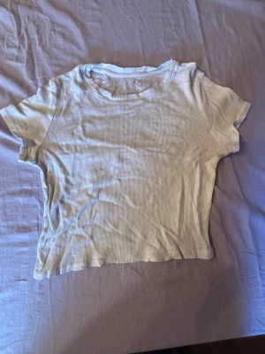 Ljusribbad croppad topp - Säljer en ljus, ribbad croppad topp med korta ärmar. Toppen har en enkel och clean look med rund halsringning och är perfekt för dig som gillar minimalistisk stil. Materialet är mjukt och stretchigt för en bekväm passform.