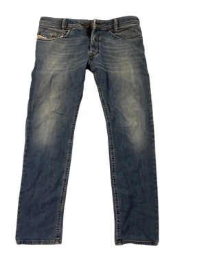 Diesel jeans - Säljer ett par blå jeans med raka ben och snygga slitningar framtill. Jeansen har klassisk femficksdesign, knappgylf och kontrastsömmar. Materialet är denim i bomull och de har en avslappnad passform som passar till det mesta.