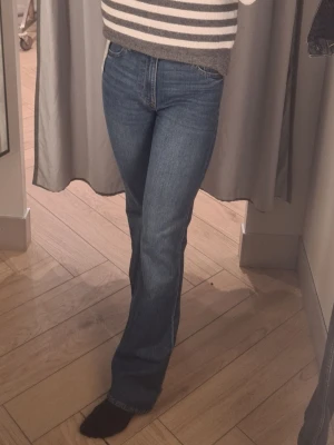 Blå bootcut jeans med hög midja - Snygga blå bootcut jeans med hög midja och klassisk femficksdesign. Jeansen har en rak passform över låren och lätt utsvängda ben. Tillverkade i denim med en autentisk tvättad look. Perfekta för en avslappnad och trendig stil.