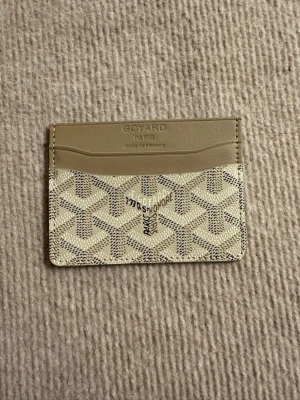 Beige kortfodral från Goy4ard - Snyggt och stilrent kortfodral från Go4ard i beige och vitt med klassiskt mönster. Tillverkat i läder och canvas med präglad logotyp och text. Perfekt för kort och ID, smidig att ha i fickan.