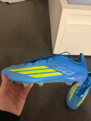 Addidas F50 ELITE FG osläppt nymodell. Storlek 44. Ny skick helt oanvända.  - Säljer ett par blåa Adidas X Speedportal som är osläppta för FIFA 26 fot med neon-gula detaljer och klassiska tre ränder på sidan.