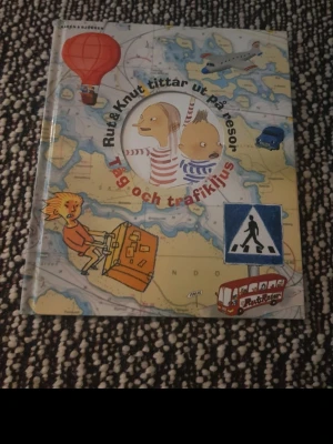 Rut & Knut tittar ut på resor - En färgglad barnbok med titeln 'Rut & Knut tittar ut på resor: Tåg och trafikljus'. Omslaget har illustrationer av barn, luftballong, flygplan, buss och vägskyltar på en karta. Perfekt för dig som gillar äventyr och trafik.