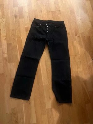 Svarta raka jeans från Levi's - Säljer ett par svarta jeans från Levi's med rak passform och knappgylf. Klassisk femficksmodell och diskret läderpatch bak i midjan. Jeansen är i ett kraftigt denimtyg och har en clean look som funkar till allt. Jeansen är smutsiga men tvättas vid säljning, är i bra skick.