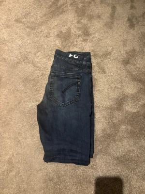Dondup George 31 - Snygga mörkblå jeans från Dondup med klassisk femficksdesign och raka ben. Jeansen har diskreta slitningar och är tillverkade i ett mjukt denimtyg som ger en bekväm passform. Perfekta för dig som gillar en enkel och stilren look. Storlek 31 är dock slitna under de sista bilden. Hör av er vid frågor