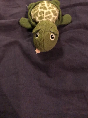 Grön mjukisdjurssköldpadda - Söt mjukisdjurssköldpadda i grönt tyg med mönstrat skal och stora broderade ögon. Sköldpaddan har fyra ben, svans och ljusgul mage. Perfekt som gosedjur eller dekoration.
