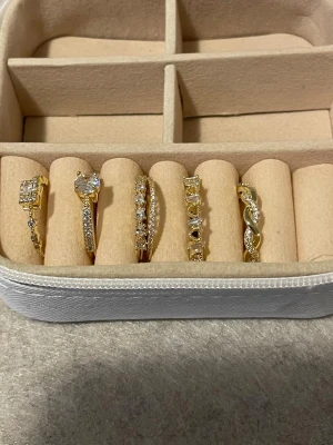 Guldpläterade i guld 18k och justerbara ringar med stenar och pärlor - Säljer ett set med fem guldpläterade ringar med gnistrande stenar i olika former och designer.  Materialet i Copper rostfritt och pläterade i 18k för bättre hållbarhet.Några ringar har större stenar i mitten medan andra har mindre stenar längs hela ringen. Perfekta för att mixa och matcha för en trendig look. Alla har öppning och kan justeras i storleken 