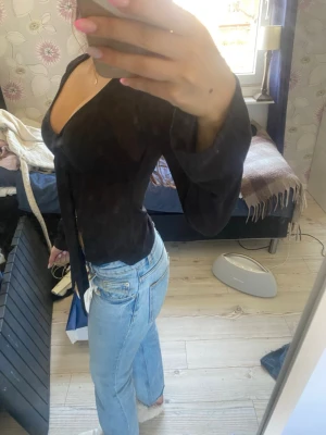 Svart omlottopp med v-ringning - Snygg svart omlottopp med v-ringning och långa ärmar. Toppen har en figurnära passform och knyts i sidan för en trendig look. Perfekt att styla med jeans eller kjol för en cool outfit.