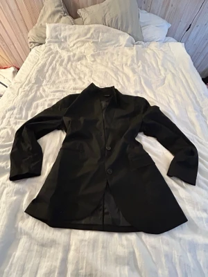 Svart klassisk kavaj med två knappar - Snygg svart kavaj med två knappar framtill och klassisk krage.. Passar perfekt till både jeans och kostymbyxor. Materialet känns slätt och har en lätt glans.