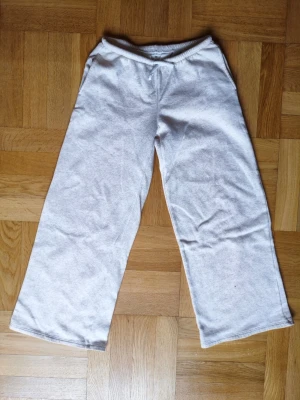 Ljusgrå vida mjukisbyxor - Ett par ljusgrå mjukisbyxor med rak och vid passform. Byxorna har resår i midjan och är tillverkade i ett mjukt och bekvämt material, perfekt för en avslappnad stil. Storlek 152