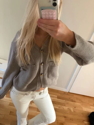 Brunbeige kofta med fickor - Mysig brun beige kofta med knappar framtill och två fickor på bröstet. Modellen är cropped och har långa ärmar samt ribbade muddar. Perfekt att slänga över en topp för en avslappnad look. Knappast använd. Storlek 34/36
