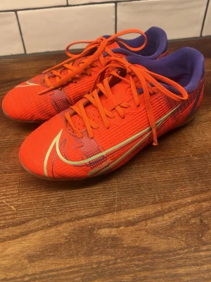 Nike Mercurial röda fotbollsskor - Säljer ett par Nike Mercurial fotbollsskor i rött med lila detaljer och silvriga sulor. Skorna har snörning och en låg profil.