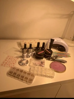 Stort nagelkit med gel och dekorationer - Säljer ett komplett nagelkit med flera geléer, nagellack, dekorationer, nagelverktyg, penslar, nagelstämplar, rhinestones och en UV-lampa. Perfekt för dig som vill fixa snygga naglar hemma. Innehåller även olika färger och former på dekorationerna samt förvaringsboxar.