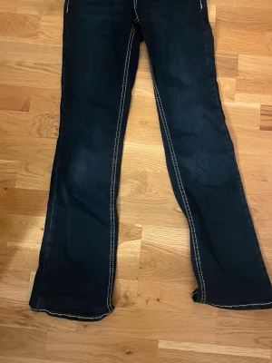 Mörkblå bootcut jeans Perfect Jeans - Säljer ett par mörkblå bootcut jeans från Gina med vita sömmar. Även dessa har glömts bort i garderoben och bara användts en gång. Inte sönder o inga slitningar. Dessa har också knappfickor och är i storlek 34.