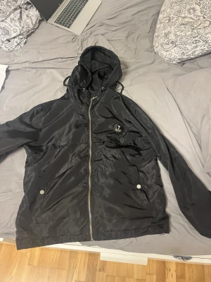 Svart vindjacka från trapstar  -  svart vindjacka från trapstar med luva  och dragkedja. . Materialet är glansigt och lätt.