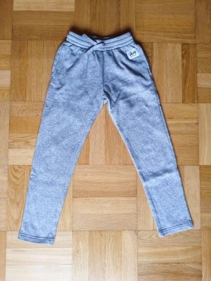 Grå mjukisbyxor med resår från Frank Dandy - Snygga grå mjukisbyxor från Frank Dandy med elastisk midja och ett litet tryckt märke framtill. Mjukt och stretchigt material som sitter skönt hela dagen. Perfekta att matcha med oversized hoodie eller t-shirt. 185:-