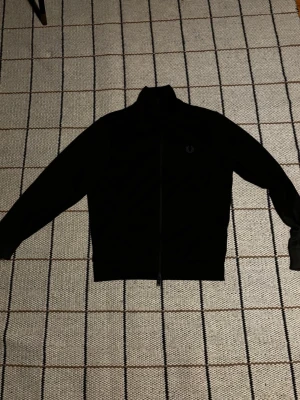 Svart zip-tröja från Fred Perry - En skön mörk grön fred Perry track zip med lite ljusare gröna ränder på ärmarna sitter riktigt skönt. Skriv vid nån fundering 
