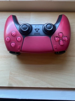 Röd PlayStation 5 DualSense handkontroll - Snygg vinröd PlayStation 5 DualSense handkontroll med klassisk design och ergonomiskt grepp. Tillverkad i plast med touchpad, inbyggd högtalare och responsiva knappar. Perfekt för gaming på PS5 och har USB-C laddning. Aldrig använd. 