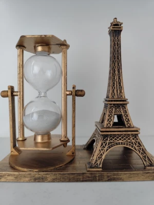 Dekorativ timglas och Eiffeltorn prydnad - Snygg prydnad i metall med ett klassiskt timglas och en detaljerad modell av Eiffeltornet i guldfärg. Perfekt som inredningsdetalj för skrivbord eller hylla. Timglaset har vitt sand och står på en gemensam bas tillsammans med tornet.