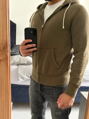 Olivgrön hoodie Polo Ralph Lauren - Mycket skön olivgrön hoodie med dragkedja från Polo Ralph Lauren i storlek S. Passar dig mellan 170-180cm. Inga defekter alls! Passar utmärkt till våren! Bara att skriva vid funderingar!🌟