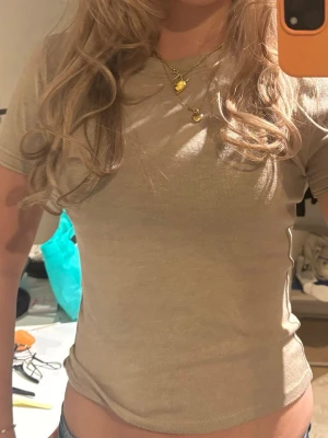 Beige ribbad t-shirt - Säljer en beige ribbad t-shirt med korta ärmar och rund hals. T-shirten har en tight passform och är tillverkad i ett mjukt bomullsmaterial som sitter snyggt på kroppen. Perfekt att matcha med jeans eller kjol för en enkel och clean look. 