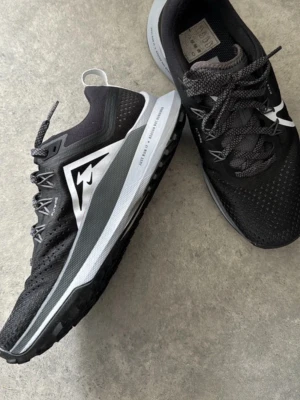 Svarta Mizuno sneakers med vit sula - Snygga svarta sneakers från Nike med vit och grå sula. Skorna har ventilerande mesh-ovandel, svarta skosnören och en tydlig Nike-logga i vitt på sidan. Perfekta för dig som gillar sportig stil och vill ha bekväma skor till vardags.