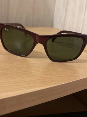 Ray-Ban brun solglasögon - Säljer ett par snygga Ray-Ban solglasögon med brun plastbåge och mörka rektangulära linser. Klassisk design som är enkel att matcha med olika outfits. Perfekt för soliga dagar och ger ett coolt intryck.