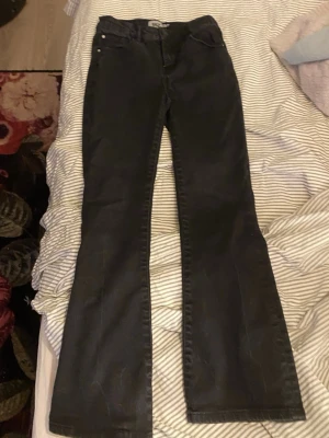 Svarta bootcut jeans - Säljer ett par svarta bootcut jeans med klassisk femficksdesign och knappstängning. Jeansen har en lätt utsvängd passform och är tillverkade i denim. Perfekta för dig som gillar en tidlös och cool look.