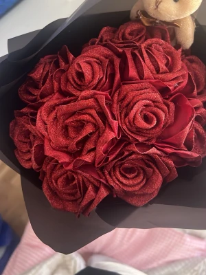 Bukett med röda konstrosor - Säljer en bukett med röda konstgjorda rosor inslagna i svart papper. Rosorna har en sammetsliknande yta och buketten har även en liten nallebjörn upptill. Perfekt som present eller dekoration.