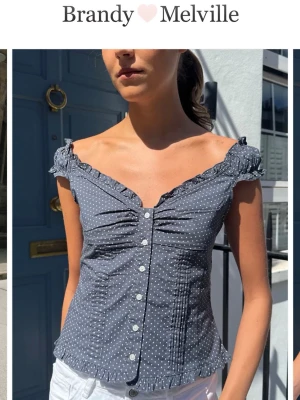 Prickig topp från Brandy Melville nyskick  - Mörkblå prickig topp med v-ringning och volangkant från Brandy Melville. Toppen är ärmlös med smockade axelband, knappar framtill och figurnära passform. Använd en gång. Så fin 