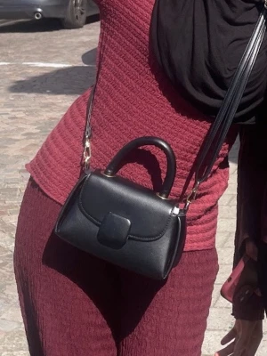 Svart axelväska i konstläder - Snygg liten svart väska med både axelrem och handtag. Använd flera gånger men fortfarande i bra skick. Säljs då jag inte använder den längre. 