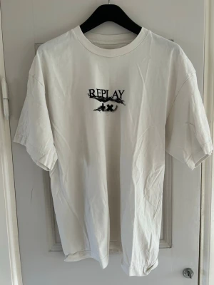 Vit t-shirt från Replay x Martin Garrix - Vit t-shirt från Replay i samarbete med Martin Garrix. Klassisk passform med korta ärmar och rund halsringning. Tryck med Replay-logga och detaljer framtill. Perfekt för en stilren och avslappnad look.