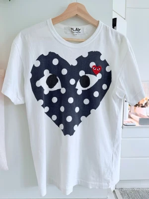 Vit Comme des Garçons t-shirt - Kvitto finns Vit t-shirt från Comme des Garçons Play med ett stort svart hjärta med vita prickar och ögon på bröstet samt en liten röd hjärtlogga. Klassisk rund hals och korta ärmar. Tillverkad i mjuk bomull för en skön känsla.
