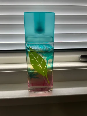 Elizabeth Arden Green Tea Tropical EdT - Fräsch parfym från Elizabeth Arden i en färgglad glasflaska med turkost lock och grön bladdekor. Flaskan har en gradient i rosa, gult och blått som ger tropiska vibbar. Perfekt för dig som gillar lätta och fruktiga dofter. Sparsamt använd 