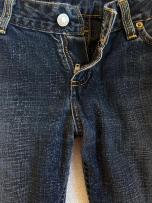 Mörkblå Levis bootcut jeans - Säljer ett par mörkblå bootcut jeans med klassisk femficksdesign och dragkedja. Jeansen har snygga slitningar och kontrastsömmar. 