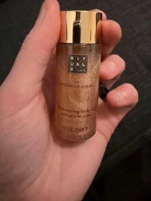 Rituals The Ritual of Karma Shimmer Oil - Glittrande kroppsolja från Rituals, The Ritual of Karma. Oljan har en skimrande guldig färg och kommer i en liten plastflaska med guldfärgat lock. Perfekt för att ge huden en snygg glow och lyster.