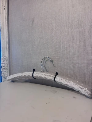 2st grå galgar med spets och prickar - Säljer 2st vadderade galgar i grått tyg med vita prickar och dekorativ vit spets längs kanten. Galgarna har metallkrok perfekt för att hänga upp fina plagg i garderoben.