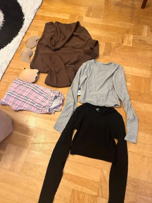 Rutig handväska med kedja - Säljer en liten handväska i klassiskt rutigt mönster med bruna, svarta, vita och röda toner. Väskan har en guldfärgad kedja och ett brunt axelband i läderimitation. Perfekt accessoar för att lyfta din outfit.  Väskor 150 kr