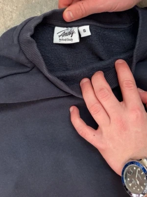 Mörkgrå hoodie från Andy by Frank Dandy - Mörkgrå hoodie från Andy by Frank Dandy med klassisk huva och ribbade muddar. Materialet är mjukt och fleeceliknande på insidan, perfekt för att hålla dig varm. Diskret logotyp på bröstet och etikett i nacken. Enkel och stilren design.