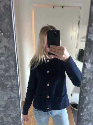 Mörkblå kofta med guldknappar - Jag säljer min marinblåa kofta från bandelid med guldknappar framtill, den har ett tjockare stickar material, man kan ha den både stängd och öppen. Den funkar lika bra till skolan som till finare tillfällen då man lätt kan stayla den☺️tror inte den säljs i butik längre heller! Nypris 799kr