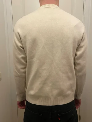 Beige stickad tröja med rund hals - En stilren beige stickad tröja med rund halsringning och ribbade muddar vid ärmslut och nederkant. Perfekt för lager-på-lager och enkel att matcha med olika outfits.