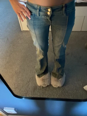 Blå jeans med dubbla knappar - Säljer ett par blå jeans med dubbla knappar i midjan och raka ben. Jeansen har en cool sömdetalj framtill och klassiska fickor. Perfekt för dig som gillar en trendig och avslappnad look.