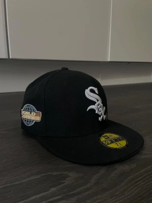 Svart White Sox keps från New Era - Säljer en svart New Era 59FIFTY keps med White Sox-logga broderad i vitt framtill och World Series-märke på sidan. Klassisk flat brim och broderad New Era-logga på sidan. Perfekt för dig som gillar sportig streetstyle.