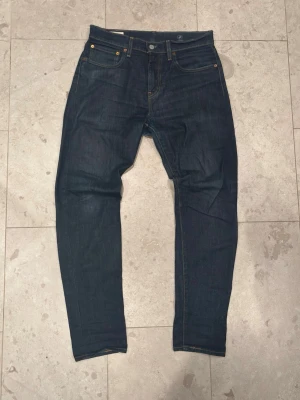 Mörkblå Levi's jeans herr size 31/32 - W31 L32Säljer ett par klassiska mörkblå jeans från Levi's med fem fickor och raka ben. Jeansen har gul kontrastsöm och en brun patch bak i midjan. Tillverkade i slitstark denim och har en tidlös look som passar till det mesta.