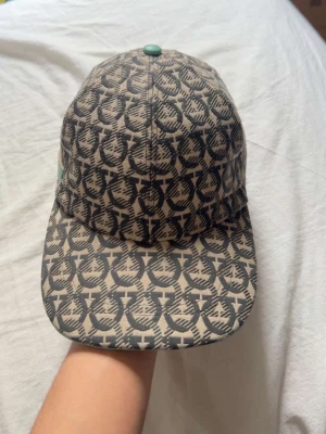 Ferragamo Keps - Snygg ferragamo keps utan några difekter alls!! Kepsen har böjd skärm och justerbar rem bak. Perfekt för dig som vill sticka ut med en unik accessoar.