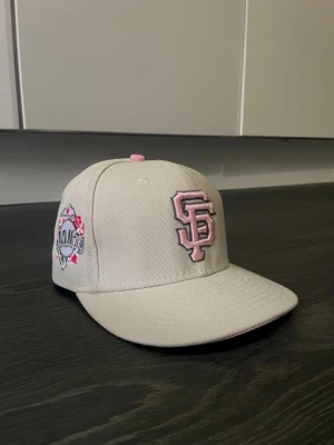 San Francisco Giants keps New Era - Snygg beige keps från New Era med San Francisco Giants logga i rosa brodyr framtill och detaljer på sidan. Klassisk flat brim och justerbar passform. Perfekt för dig som vill ha en stilren och sportig look med en touch av rosa.