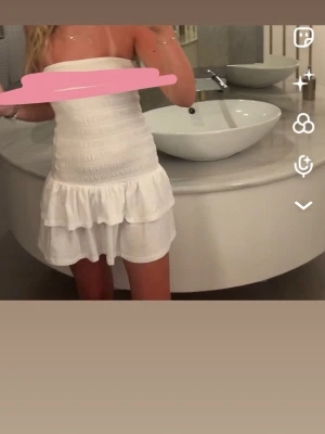 Vit bandeauklänning Gina Tricot XS - Supersöt vit bandeauklänning från Gina Tricot i storlek XS. Klänningen är kort, har volangdetaljer nertill och är axelbandslös. Perfekt för varma dagar och har en smockad, figurnära passform.