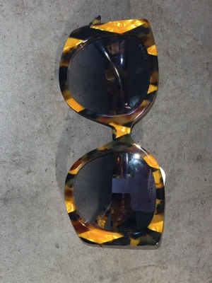 Gucci solglasögon i sköldpaddsmönster - Säljer ett par statement solglasögon från Gucci med stort, fyrkantigt sköldpaddsmönstrat plastbåge i brunt och gult. Mörka linser och guldfärgade Gucci-loggor på skalmarna. Perfekta för dig som vill sticka ut och addera lyx till din look.