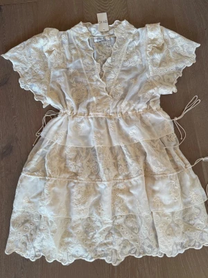 BYIC klänning i stl S helt ny studentklänning - Kort spetsklänning med unik vintagelook, volangdetaljer. Djup halsringning vid bröstet. Möjlighet till justering i midjan och i nedre delen av klänningen.  Helt ny