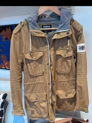 Bonfeild Cardigan beige  - Stilren beige cardigan från Bondelid med fyra stora fickor framtill, tyvvär är det en knapp som har hoppat sönder på en utan vänster framficka med det syns inte, ej använd då jag har för mycket kläder som ligger. Mvh Malte