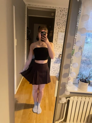 Brun kortkjol med volang - Säljer en brun kortkjol med volangdetaljer. Kjolen har en utsvängd form. Materialet känns mjukt och lätt, gjord i polyester.